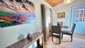 A room with a wooden ceiling, a colorful abstract painting, a bench, a dining table with chairs, and a blue door. - The Redwood Hearts Cottage in Cambria (Cambria)