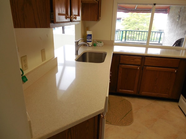 A kitchen with wooden cabinets, a stainless steel sink, and a window overlooking a balcony.