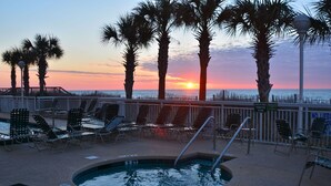 A pool area with lounge chairs and a hot tub, surrounded by palm trees and a sunset view. - Oceanfront End Unit 4BR 3BA Sleeps 12 75 Inch TV Crescent Shores N Myrtle Beach (North Myrtle Beach)