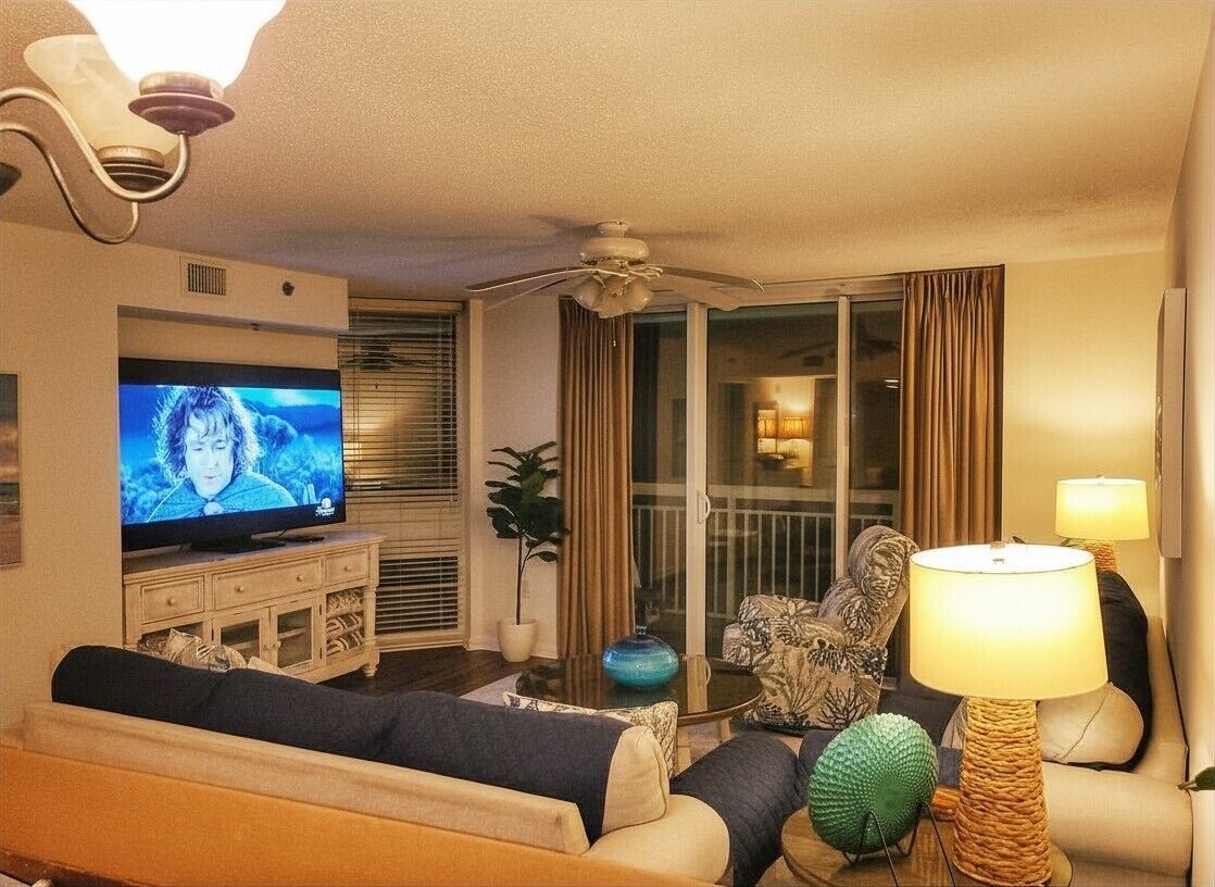 A living room with a television, sofa, armchair, lamp, and a ceiling fan.