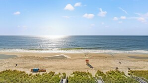 A beach with a lifeguard tower, a boardwalk, and a grassy area in the foreground. - Oceanfront End Unit 4BR 3BA Sleeps 12 75 Inch TV Crescent Shores N Myrtle Beach (North Myrtle Beach)