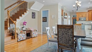 A spacious living room with a wooden staircase, a dining area with patterned chairs, and a kitchen with wooden cabinets and a microwave.