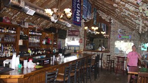 Eine Bar mit Holztresen, mehreren Sitzbereichen und einer Backsteinwand mit verschiedenen Schildern und Dekorationen.