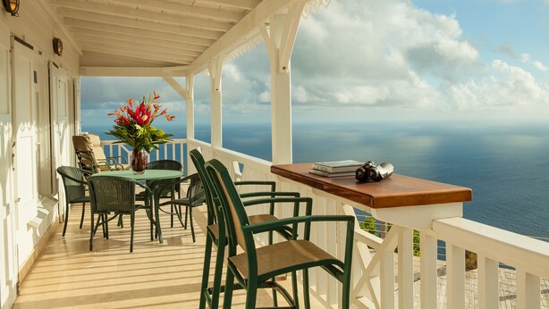 A covered outdoor area with a table and chairs, a vase with flowers, and a view of the sea.