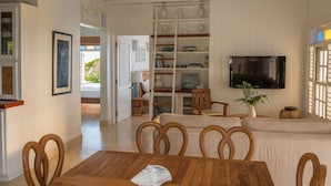 A living room with a wooden dining table, chairs, a sofa, and a TV mounted on the wall.