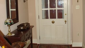 Un couloir avec une porte blanche, un escalier en bois, un miroir et une petite table avec une lampe.