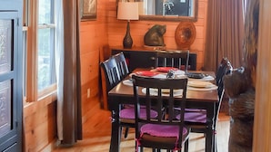 L'intérieur d'un chalet en bois, avec une table à manger dressée pour quatre personnes, un lustre, un miroir et une grande fenêtre.