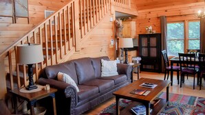 L’intérieur d’un chalet en bois comprend un escalier, un canapé en cuir, une table à manger et un buffet.