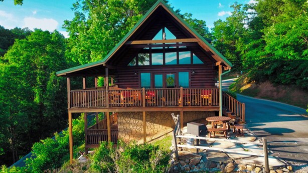 Une cabane en bois dotée d’un balcon, de fondations en pierre et d’un espace extérieur aménagé pour s’asseoir.