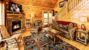 L’intérieur chaleureux d’un chalet en bois, avec une cheminée en pierre, un plancher en bois, un coin salon confortable et un escalier menant à un étage supérieur.