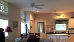 Una sala de estar con sofá, reposapiés y una mesita. Hay una zona de cocina con mostrador, fregadero y armarios.
