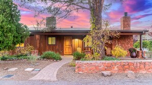Une maison en bois avec une cheminée en pierre, une porte en bois et un chemin en briques menant à l’entrée.