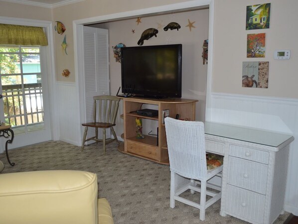 A room with a television on a wooden stand, a white wicker chair, a small desk, and a yellow couch. - Home With Cottage Feel Offering Golf Cart, Kayaks, Bikes, Fishing (Goodland)