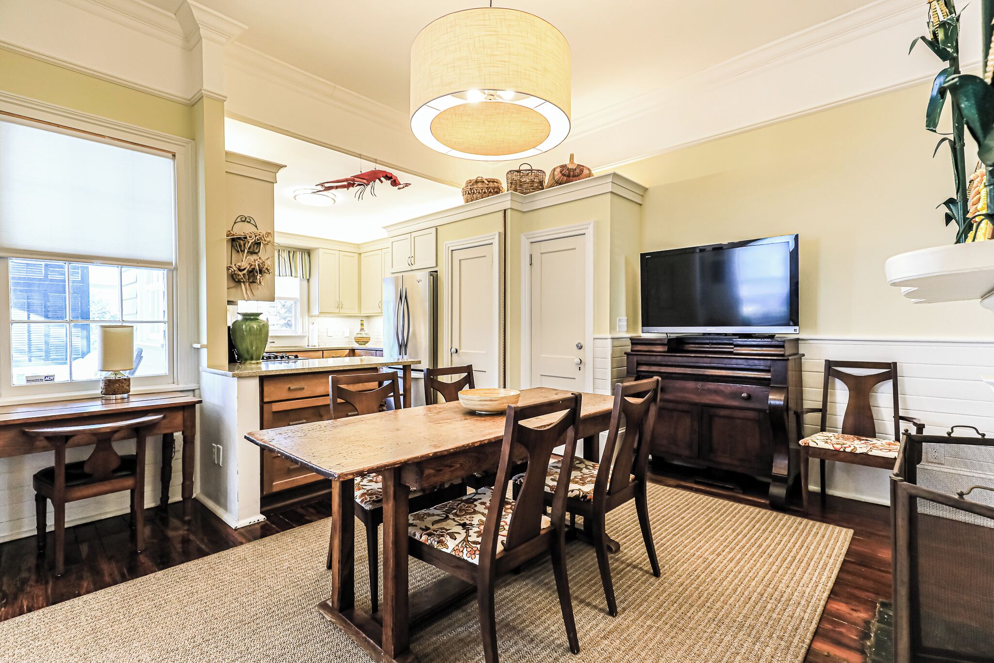 A dining area with a wooden table and chairs, a chandelier, and a television on a stand.