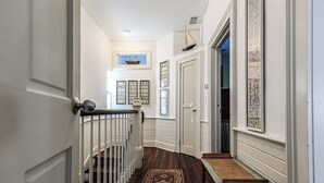A hallway with a wooden floor, white walls, a white door, and a small bench. - Jingle Bells Square House (Savannah)