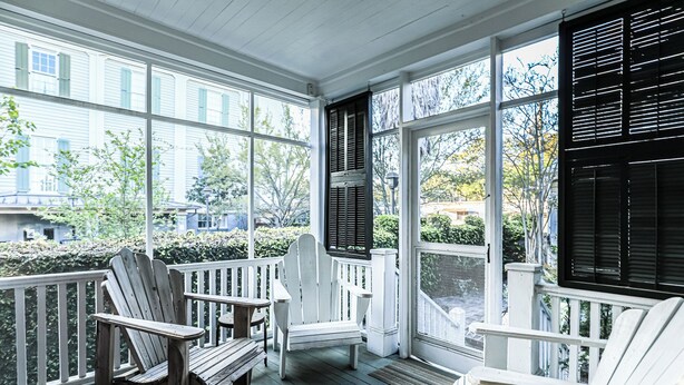 A covered porch with white Adirondack chairs and a bench, large windows, and a view of the neighborhood. - Jingle Bells Square House (Savannah)