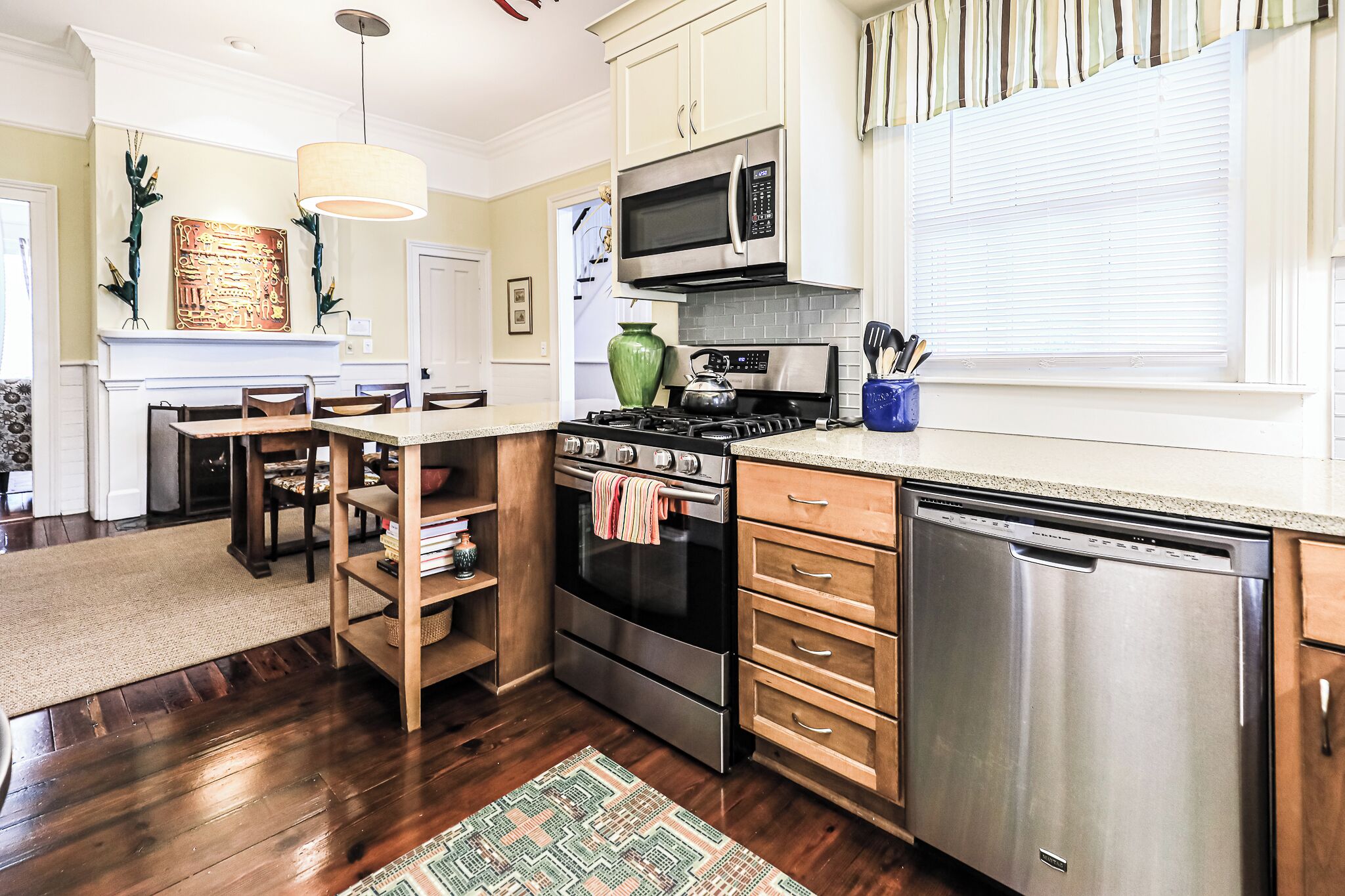 A modern kitchen with stainless steel appliances, wooden cabinets, and a dining area with a rug and chairs.