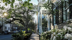 A street lined with trees and parked cars, with a building featuring a balcony and a hanging light fixture. - Jingle Bells Square House (Savannah)