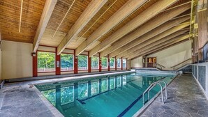 Une piscine intérieure dotée d’un haut plafond en bois, d’un sol en pierre et offrant une vue sur les arbres à travers de grandes fenêtres.