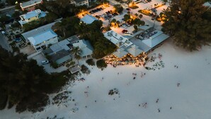 An aerial view of a resort with multiple buildings, a parking area, and a beach with people.