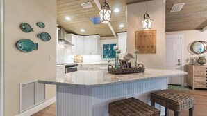 A kitchen with a large island, pendant lights, and decorative fish plates on the wall.