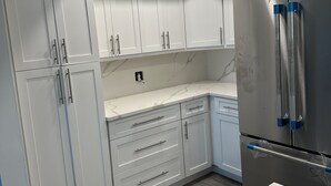 Eine moderne Küche mit weißen Schränken, einem Edelstahlkühlschrank und einer Marmorarbeitsplatte.