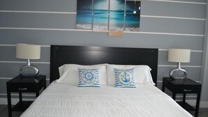 Ein ordentlich eingerichtetes Schlafzimmer mit einem großen Bett, zwei Nachttischen und einem Wandbild, das eine Strandansicht zeigt.