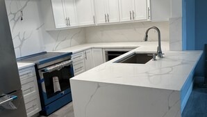 Eine moderne Küche mit weißen Schränken, einem eingebauten Ofen und einer großen Kochinsel mit Spüle.