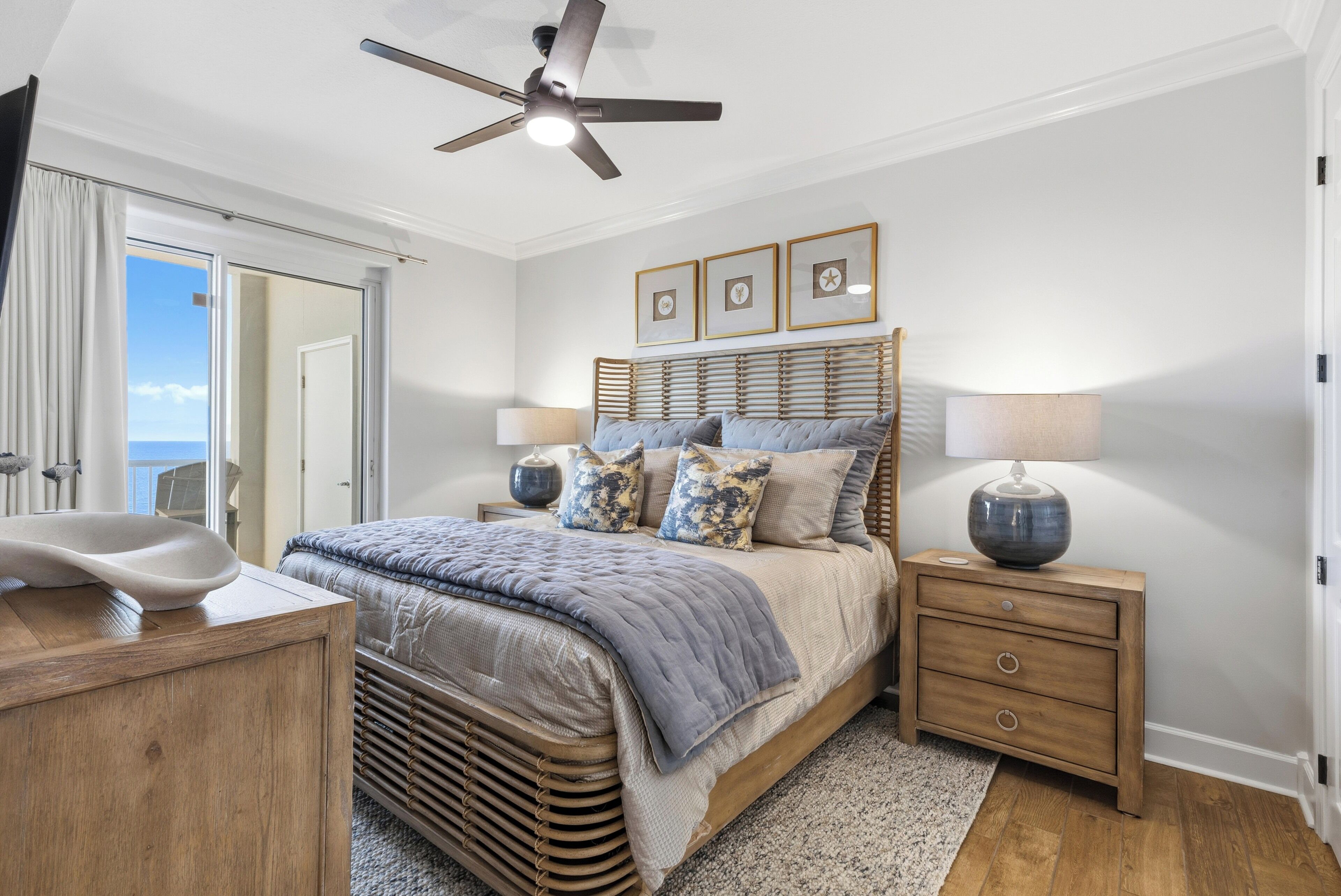 A bedroom with a bed, bedside tables, a ceiling fan, and a view of the outdoors.