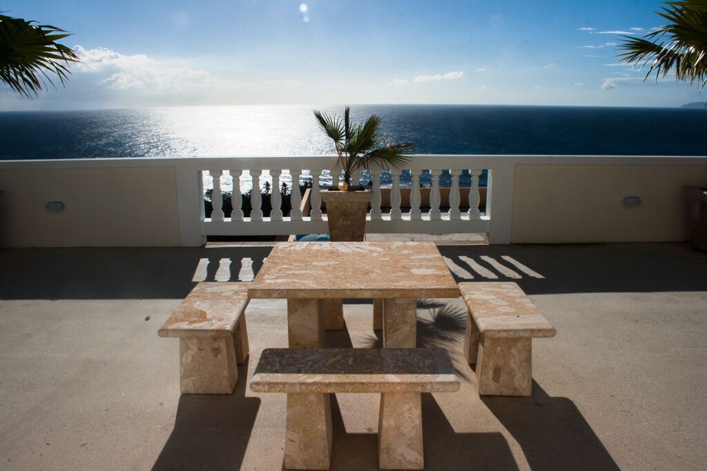 A terrace with a table and benches, overlooking a body of water.