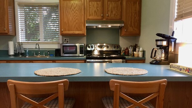 Una cocina con gabinetes de madera, un microondas, estufa y dos taburetes de bar.