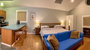 Un dormitorio compacto con cama, sofá azul, pequeña kitchenette y chimenea.