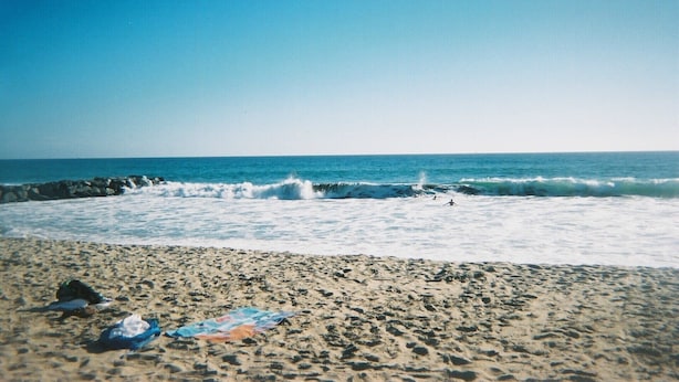 A beach with waves, a clear sky, and a rocky shoreline.