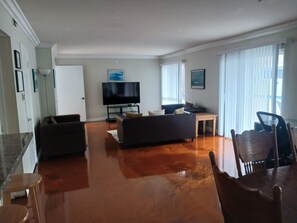Ein Wohnzimmer mit einer Couch, einem Fernseher, einem Esstisch und Stühlen.