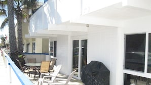 An outdoor patio with a table and chairs, a covered grill, and a trash can.