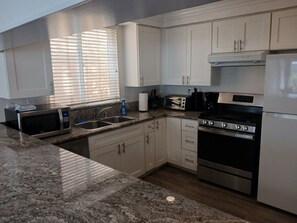 A modern kitchen with white cabinets, granite countertops, a stove, microwave, and a toaster.