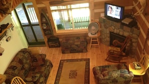 Een gezellige woonkamer met houten vloer, een sofa met patroon, een houten stoel, een kleine tafel en een televisie aan een stenen muur.