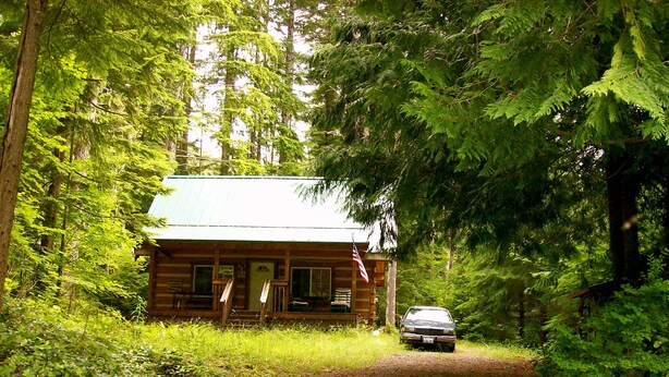 Een chalet met een veranda, een voertuig ervoor geparkeerd, omgeven door dicht bos.