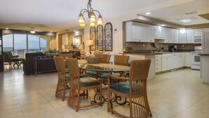 A spacious kitchen with white cabinets, a dining area with wicker chairs and a glass table, and a view of the ocean through large windows. - Luxurious Oceanview Condo in Cozumel (Cozumel, Centre)