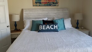 A neatly made bed with a white quilt, two nightstands with lamps, and a wall painting of a car. - La Casita-Oceanfront Oasis with Great Views (Carolina Beach)