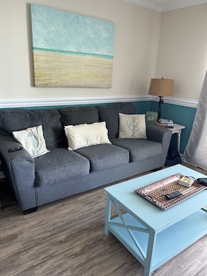 A living room with a grey sofa, a light blue coffee table, and a teal wall.