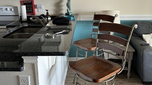 A kitchen with a sink, stove, and a bar area with two stools. - La Casita-Oceanfront Oasis with Great Views (Carolina Beach)