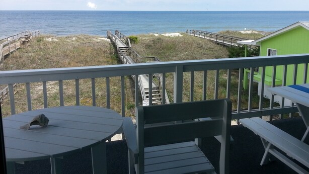A balcony with a view of the ocean, a green building, and a wooden deck. - La Casita-Oceanfront Oasis with Great Views (Carolina Beach)