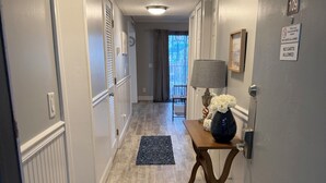 A hallway with a wooden floor, a table with a lamp, and a door with a sign.
