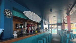 A bar with a wooden counter and blue stools, a menu board, and a logo on the wall.