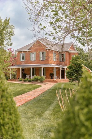A two-story brick house with a front porch, a lawn, and a pathway leading to the entrance.