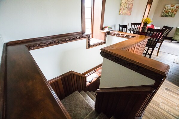 A wooden staircase with a handrail, leading to a dining area with chairs and a table.