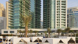 A beachfront hotel with multiple high-rise buildings in the background, outdoor seating areas with white canopies, and a sandy beach. - * Stunning! 5*- 4 BR-Oceanfront-Apartment-Private Beach- Ocean Views*  (Dubai)