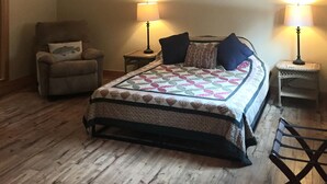 Ein Schlafzimmer mit einem Bett, zwei Nachttischlampen, einem Sessel, einem Deckenventilator und Holzboden.