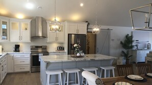 Una cocina moderna con armarios blancos, electrodomésticos de acero inoxidable y una isla central con taburetes de bar.